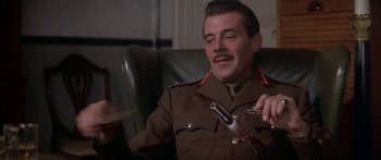 Movie still from “A Bridge Too Far” (1977), directed by Richard Attenborough – A man in a uniform sitting in a chair holding a cell phone; Close Up shot, Low angle