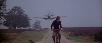 Movie still from “A Bridge Too Far” (1977), directed by Richard Attenborough – A man riding a bike down the middle of a road; Wide shot, Low angle