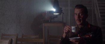 Movie still from “A Bridge Too Far” (1977), directed by Richard Attenborough – A person holding a cup of coffee in front of a projector; Medium shot, Low angle