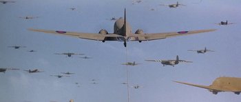 Movie still from “A Bridge Too Far” (1977), directed by Richard Attenborough – An airplane is flying in the sky over a bunch of planes; Extreme Wide shot, Low angle