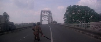 Movie still from “A Bridge Too Far” (1977), directed by Richard Attenborough – A man walking across a bridge holding an umbrella; Wide shot, Low angle