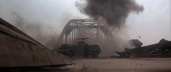 Movie still from “A Bridge Too Far” (1977), directed by Richard Attenborough – An old car is on a bridge in the middle of the day; Wide shot, Low angle