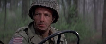 Movie still from “A Bridge Too Far” (1977), directed by Richard Attenborough – A man wearing a helmet and holding a steering wheel; Close Up shot, Over the shoulder angle