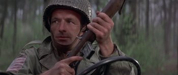 Movie still from “A Bridge Too Far” (1977), directed by Richard Attenborough – A man holding a rifle in his hand and wearing an army helmet; Close Up shot, Low angle