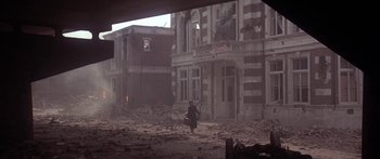 Movie still from “A Bridge Too Far” (1977), directed by Richard Attenborough – A woman walking through the rubble of a destroyed building; Extreme Wide shot, Low angle