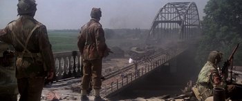 Movie still from “A Bridge Too Far” (1977), directed by Richard Attenborough – A soldier standing on the side of a bridge; Wide shot, Over the shoulder angle
