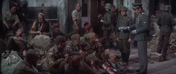Movie still from “A Bridge Too Far” (1977), directed by Richard Attenborough – A group of men sitting next to each other on the ground; Wide shot, High angle