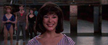 Movie still from “A Chorus Line” (1985), directed by Richard Attenborough – A woman with brown hair wearing a purple and white striped shirt; Close Up shot, Over the shoulder angle