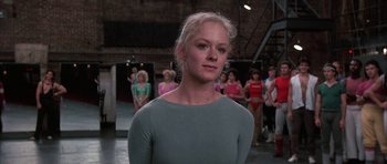 Movie still from “A Chorus Line” (1985), directed by Richard Attenborough – A woman standing in front of a group of people; Medium shot, Over the shoulder angle