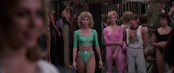 Movie still from “A Chorus Line” (1985), directed by Richard Attenborough – A woman in a pink and green outfit standing next to another woman; Medium shot, Over the shoulder angle