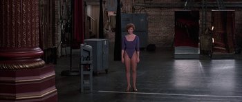 Movie still from “A Chorus Line” (1985), directed by Richard Attenborough – A woman in a purple leotard standing in a room; Wide shot, Over the shoulder angle