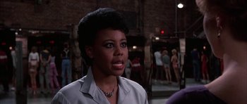 Movie still from “A Chorus Line” (1985), directed by Richard Attenborough – A black woman with short black hair wearing a white shirt; Close Up shot, Over the shoulder angle