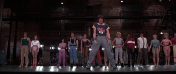 Movie still from “A Chorus Line” (1985), directed by Richard Attenborough – A group of people standing on a stage in front of lights; Wide shot, Low angle