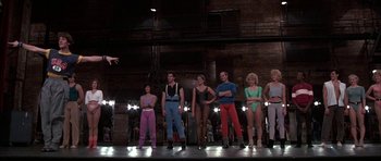 Movie still from “A Chorus Line” (1985), directed by Richard Attenborough – A group of people standing on a stage in front of lights; Wide shot, Low angle