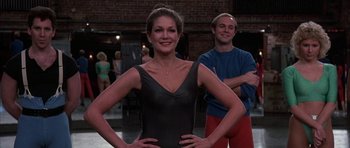 Movie still from “A Chorus Line” (1985), directed by Richard Attenborough – A woman standing next to a man in a blue shirt; Medium shot, Low angle