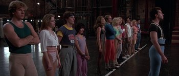 Movie still from “A Chorus Line” (1985), directed by Richard Attenborough – A group of people standing on a stage in front of a crowd; Wide shot, Low angle