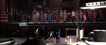 Movie still from “A Chorus Line” (1985), directed by Richard Attenborough – A group of people standing on a stage in front of an audience; Wide shot, High angle