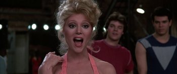 Movie still from “A Chorus Line” (1985), directed by Richard Attenborough – A woman with a surprised look on her face and a man in the background; Close Up shot, Low angle