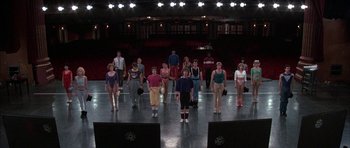 Movie still from “A Chorus Line” (1985), directed by Richard Attenborough – A group of people standing on a stage in front of lights; Wide shot, High angle