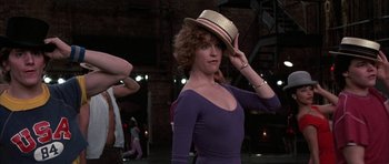 Movie still from “A Chorus Line” (1985), directed by Richard Attenborough – A woman in a purple dress and a hat; Medium shot, Over the shoulder angle