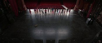 Movie still from “A Chorus Line” (1985), directed by Richard Attenborough – A group of people standing in a row in a theater; Extreme Wide shot, Overhead angle