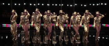 Movie still from “A Chorus Line” (1985), directed by Richard Attenborough – A group of people in gold outfits and top hats; Wide shot, Low angle