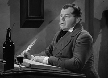 Movie still from “A Christmas Carol” (1938), directed by Edwin L. Marin – An older man sitting at a desk writing with a quill pen; Medium shot, High angle
