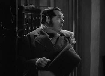 Movie still from “A Christmas Carol” (1938), directed by Edwin L. Marin – A man in a coat and tie holding a bag; Medium shot, Over the shoulder angle