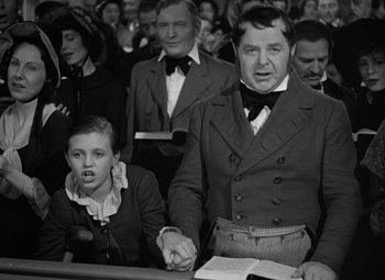 Movie still from “A Christmas Carol” (1938), directed by Edwin L. Marin – An old photo of a man and a young boy in a courtroom; Medium shot, Over the shoulder angle