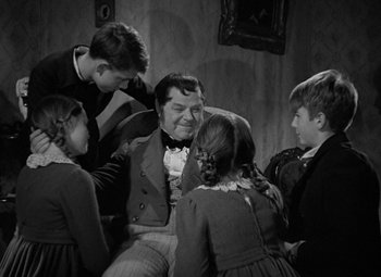 Movie still from “A Christmas Carol” (1938), directed by Edwin L. Marin – A group of people gathered around a man in a room; Medium shot, Over the shoulder angle