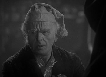 Movie still from “A Christmas Carol” (1938), directed by Edwin L. Marin – An older man wearing a hat and looking at the camera; Close Up shot, Over the shoulder angle