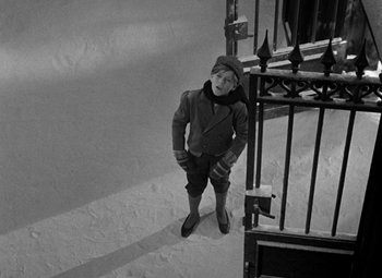 Movie still from “A Christmas Carol” (1938), directed by Edwin L. Marin – A man standing in the snow next to an iron gate; Wide shot, High angle