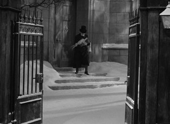 Movie still from “A Christmas Carol” (1938), directed by Edwin L. Marin – A man in a top hat holding a guitar in front of a building; Wide shot, High angle