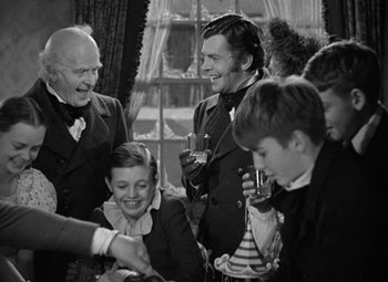 Movie still from “A Christmas Carol” (1938), directed by Edwin L. Marin – A group of people standing next to each other in front of a window; Medium shot, Over the shoulder angle