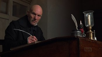 Movie still from “A Christmas Carol” (1999), directed by David Hugh Jones – An older man writing on a paper with a feather pen; Medium shot, Low angle