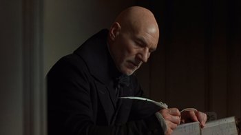Movie still from “A Christmas Carol” (1999), directed by David Hugh Jones – A bald man in a black coat is holding scissors; Close Up shot, Low angle