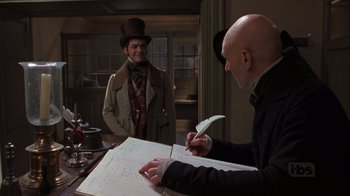 Movie still from “A Christmas Carol” (1999), directed by David Hugh Jones – A man writing on a piece of paper next to another man wearing a top hat; Medium shot, Over the shoulder angle