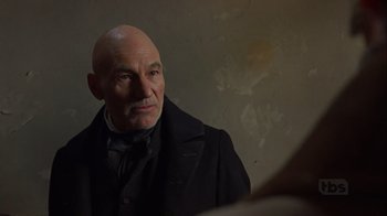Movie still from “A Christmas Carol” (1999), directed by David Hugh Jones – An older man with a bald head wearing a black coat; Close Up shot, Over the shoulder angle