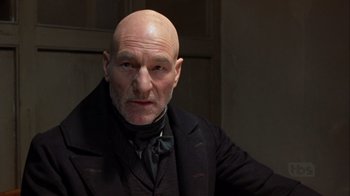 Movie still from “A Christmas Carol” (1999), directed by David Hugh Jones – A man with a bald head wearing a suit and tie; Close Up shot, Low angle