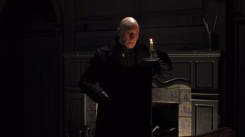 Movie still from “A Christmas Carol” (1999), directed by David Hugh Jones – A bald man holding a lit candle in a dark room; Medium shot, Low angle