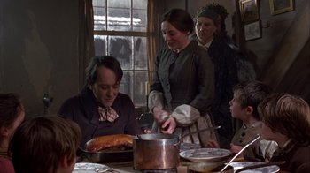 Movie still from “A Christmas Carol” (1999), directed by David Hugh Jones – A group of people sitting around a table with food on it; Medium shot, Over the shoulder angle