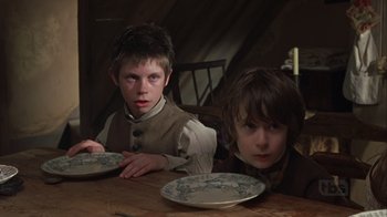 Movie still from “A Christmas Carol” (1999), directed by David Hugh Jones – Two young boys sitting at a table with plates; Medium shot, Low angle
