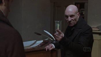 Movie still from “A Christmas Carol” (1999), directed by David Hugh Jones – A bald man in a black suit holding a glass; Medium shot, Low angle