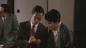 Movie still from “A City of Sadness” (1989), directed by Hsiao-Hsien Hou – Two men in business suits looking at a cell phone; Medium shot, High angle
