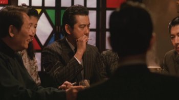 A man sitting at a table smoking a cigarette in front of other people
