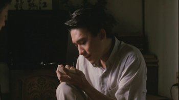 Movie still from “A City of Sadness” (1989), directed by Hsiao-Hsien Hou – A man sitting on the ground holding a cell phone; Medium shot, Low angle