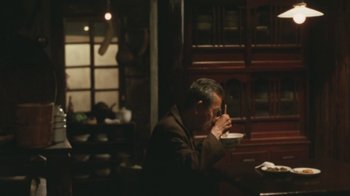 Movie still from “A City of Sadness” (1989), directed by Hsiao-Hsien Hou – A man sitting at a table drinking a cup of coffee; Medium shot, Over the shoulder angle