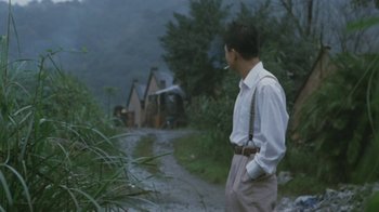 Movie still from “A City of Sadness” (1989), directed by Hsiao-Hsien Hou – A man standing on the side of a road smoking a cigarette; Medium shot, Over the shoulder angle