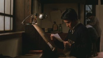 Movie still from “A City of Sadness” (1989), directed by Hsiao-Hsien Hou – A man is looking at a piece of paper in a dark room; Medium shot, Low angle