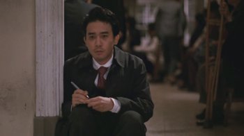 Movie still from “A City of Sadness” (1989), directed by Hsiao-Hsien Hou – A man sitting on the ground holding a pen; Medium shot, High angle